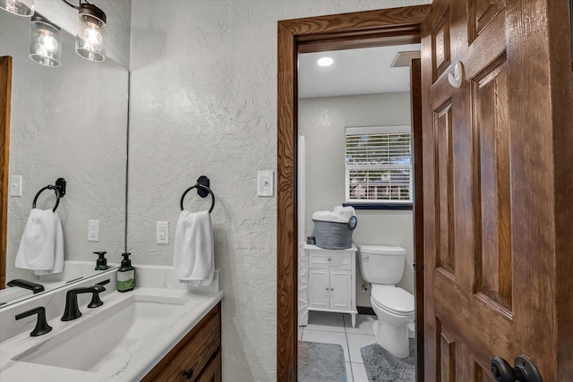 bathroom with toilet, tile patterned floors, a textured wall, and vanity
