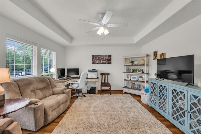 living area with a ceiling fan, a tray ceiling, and wood finished floors