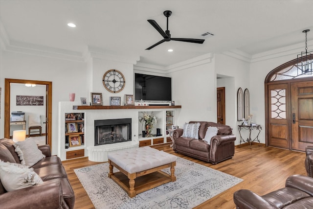 living room with visible vents, ornamental molding, a brick fireplace, wood finished floors, and a ceiling fan