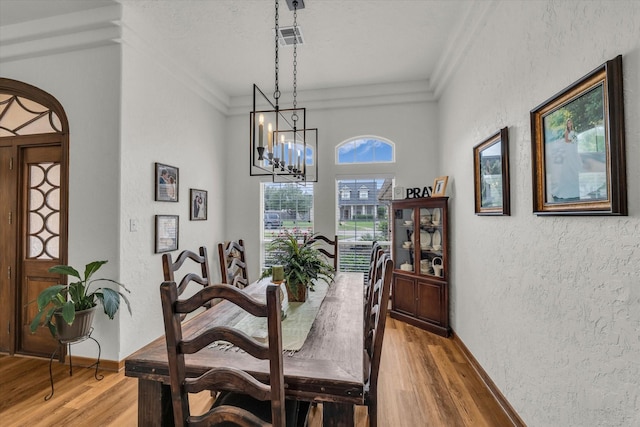 dining space with crown molding, a textured wall, an inviting chandelier, and light wood-type flooring