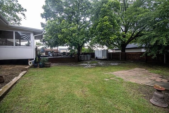 view of yard with a storage shed, a sunroom, a fenced backyard, an outbuilding, and a patio area