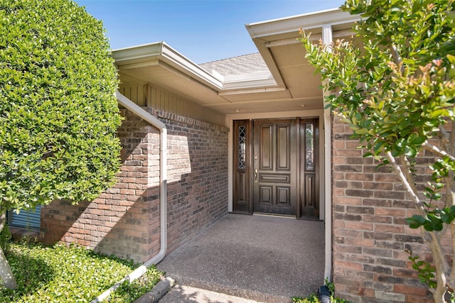 entrance to property featuring brick siding and roof with shingles
