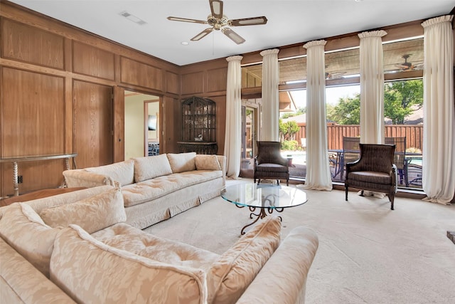 living area featuring wooden walls, a ceiling fan, light colored carpet, and visible vents