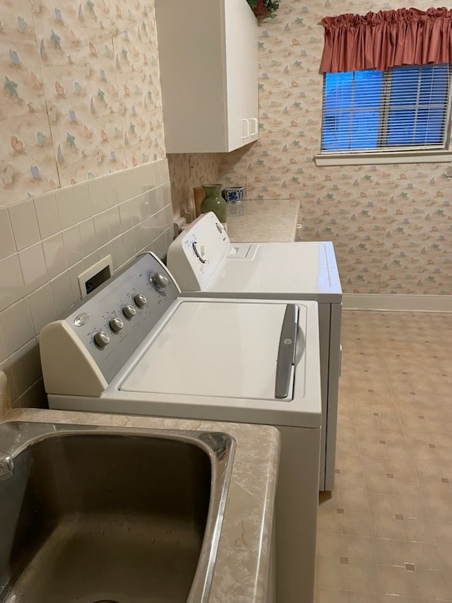 washroom featuring cabinet space, baseboards, wallpapered walls, tile walls, and washer and clothes dryer