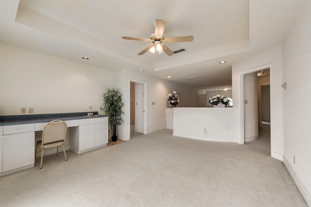 interior space featuring visible vents, built in study area, light colored carpet, a tray ceiling, and a ceiling fan