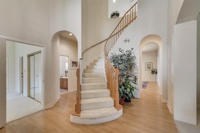 foyer entrance featuring baseboards, light wood finished floors, a towering ceiling, and stairs