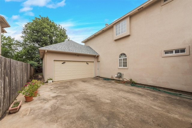 view of property exterior featuring stucco siding, a shingled roof, fence, and driveway