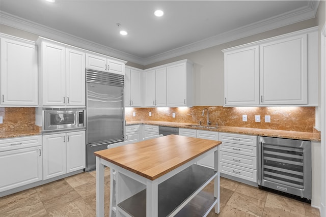kitchen with wine cooler, built in appliances, white cabinets, and a sink