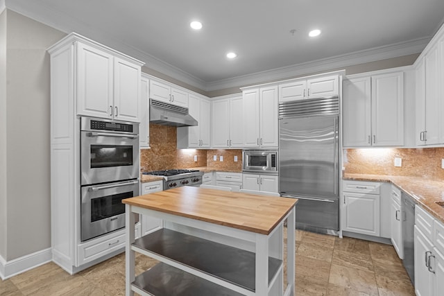 kitchen featuring built in appliances, white cabinetry, under cabinet range hood, ornamental molding, and butcher block counters