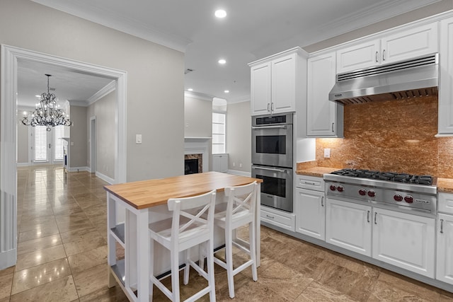kitchen with decorative backsplash, crown molding, appliances with stainless steel finishes, butcher block counters, and under cabinet range hood