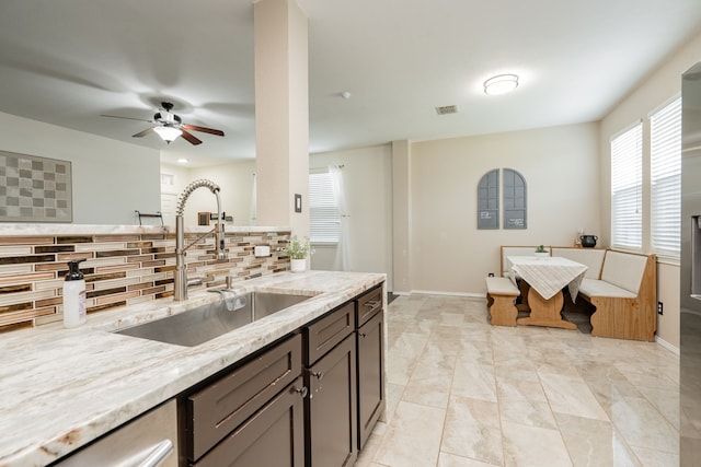 kitchen featuring ceiling fan, light stone countertops, a sink, tasteful backsplash, and visible vents