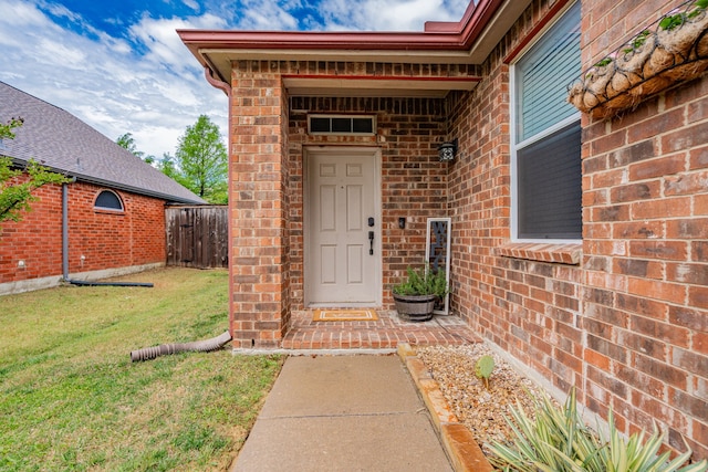 property entrance featuring brick siding, fence, and a yard