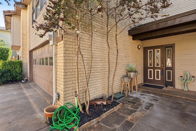 entrance to property with brick siding, a garage, and aphalt driveway