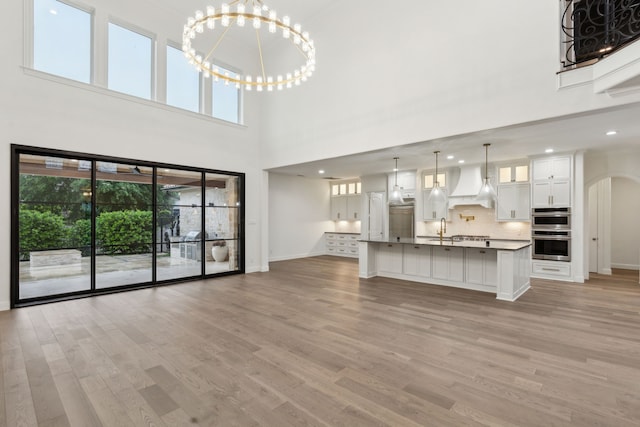 unfurnished living room with a sink, baseboards, light wood finished floors, and a towering ceiling