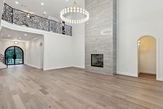 unfurnished living room featuring arched walkways, wood finished floors, baseboards, an inviting chandelier, and a high ceiling
