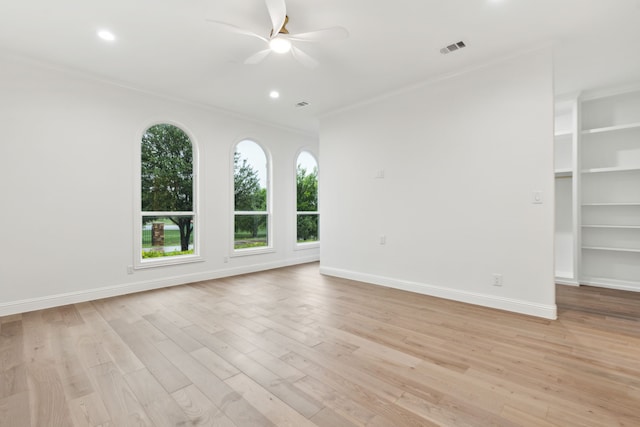 empty room featuring a ceiling fan, visible vents, ornamental molding, and light wood finished floors