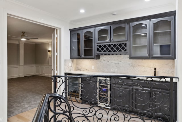 bar featuring ceiling fan, backsplash, a bar, ornamental molding, and a decorative wall
