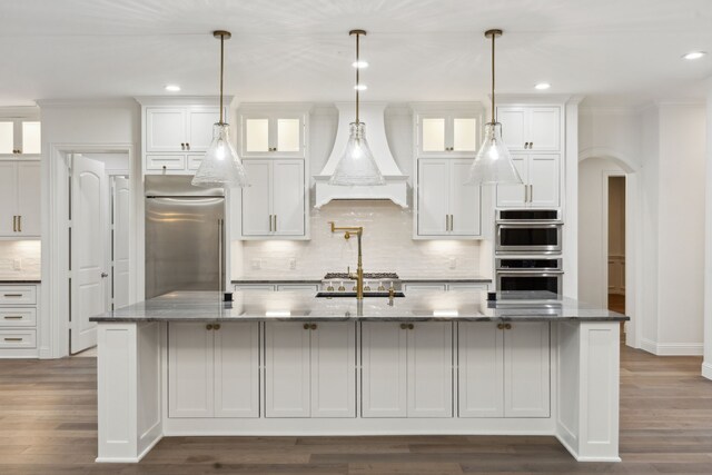kitchen with white cabinets, arched walkways, appliances with stainless steel finishes, and custom range hood