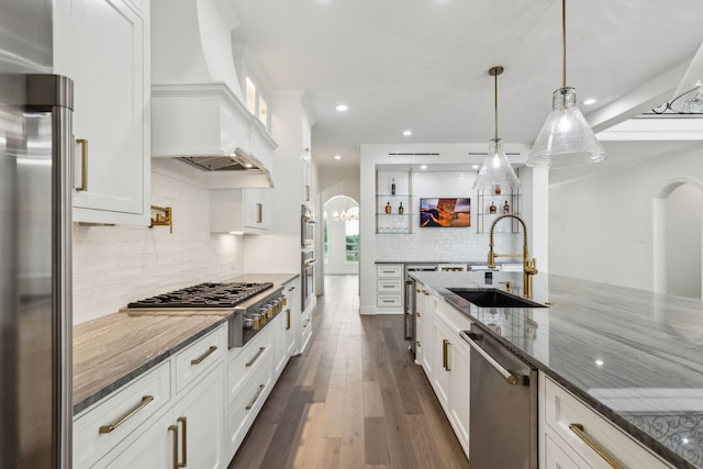 kitchen featuring a sink, appliances with stainless steel finishes, custom range hood, and dark stone counters