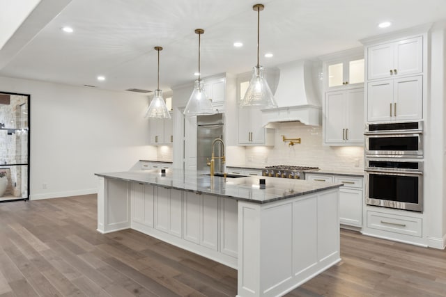 kitchen featuring decorative backsplash, appliances with stainless steel finishes, a sink, custom exhaust hood, and white cabinetry