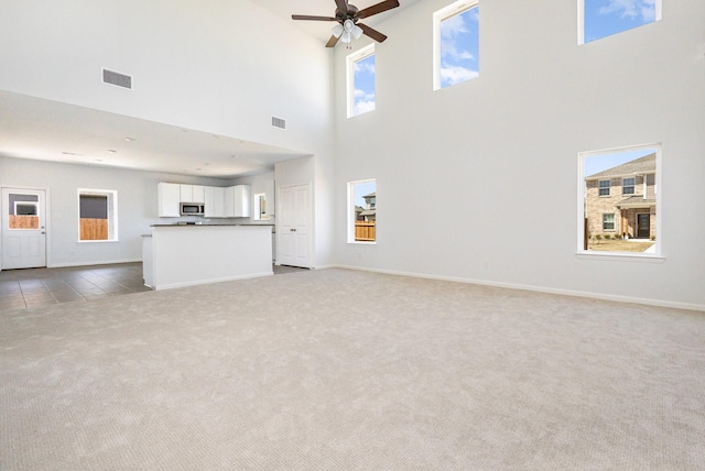 unfurnished living room with a towering ceiling, a wealth of natural light, light carpet, and visible vents