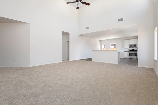 unfurnished living room with a high ceiling, light carpet, a ceiling fan, baseboards, and visible vents
