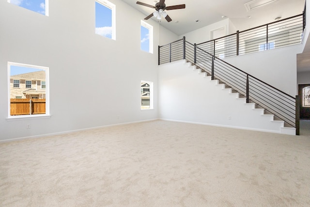 unfurnished living room featuring carpet, a towering ceiling, stairway, and ceiling fan