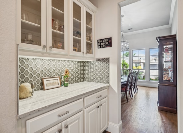 bar area with dark wood-type flooring, crown molding, backsplash, and a chandelier