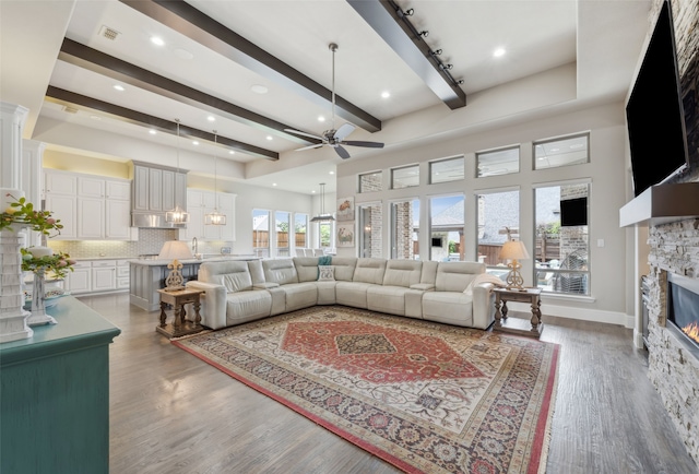 living area with a ceiling fan, a fireplace, beam ceiling, wood finished floors, and baseboards