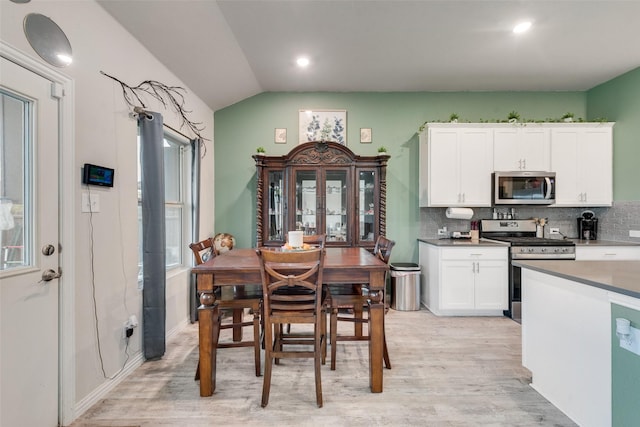 kitchen featuring lofted ceiling, white cabinetry, tasteful backsplash, light wood finished floors, and stainless steel appliances