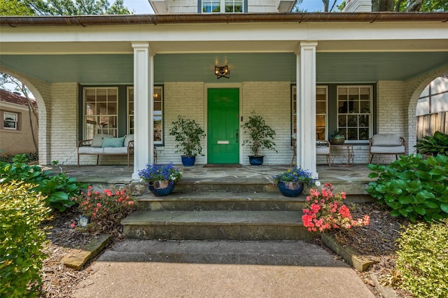 doorway to property with a porch and brick siding