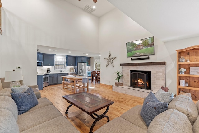 living area featuring light wood-style floors, high vaulted ceiling, visible vents, and a fireplace