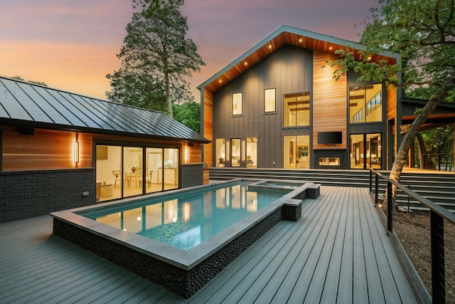rear view of house featuring a deck, a pool with connected hot tub, a standing seam roof, and metal roof