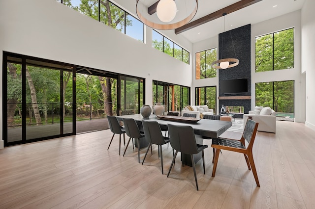 dining room featuring light wood-style floors, beam ceiling, and a towering ceiling