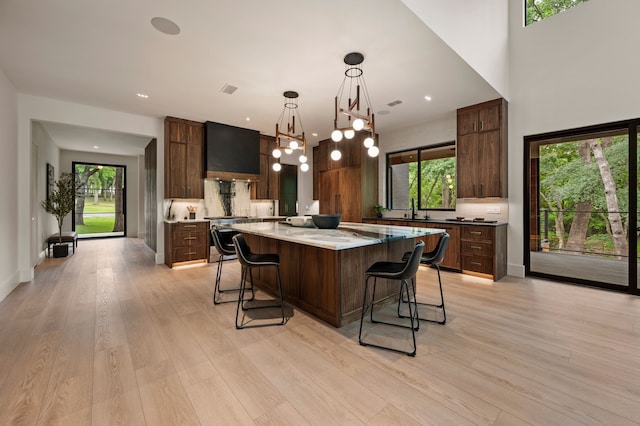 kitchen featuring a kitchen bar, a large island, light wood-type flooring, stainless steel stove, and a sink