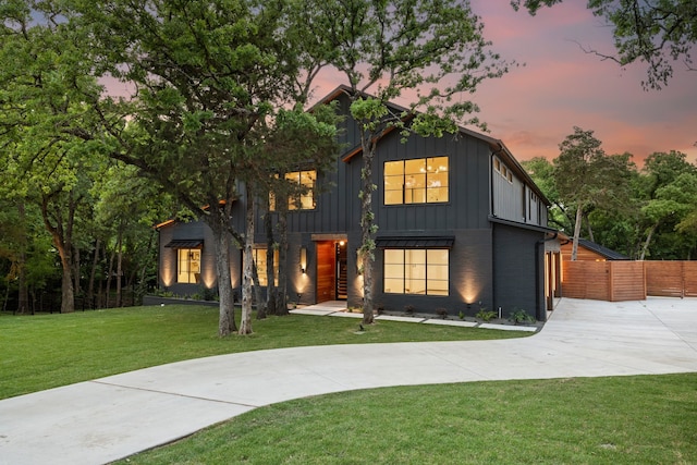 modern farmhouse featuring a lawn, curved driveway, board and batten siding, and fence