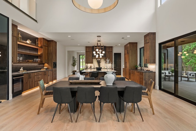 dining room featuring beverage cooler, light wood finished floors, a high ceiling, and a chandelier