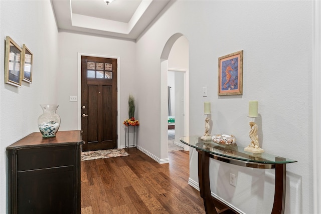 entrance foyer featuring arched walkways, baseboards, a tray ceiling, and dark wood-type flooring