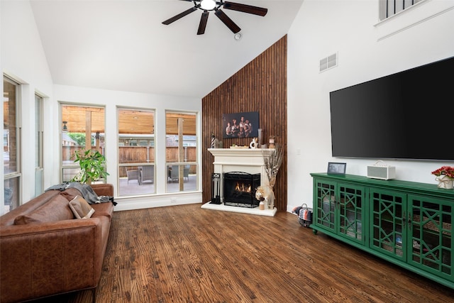 living room with a ceiling fan, visible vents, wood finished floors, high vaulted ceiling, and a warm lit fireplace