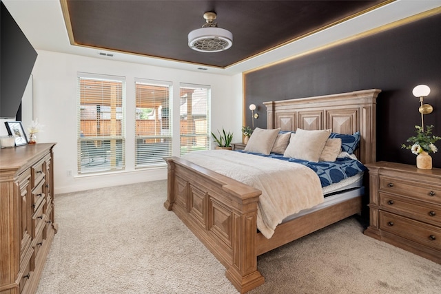 bedroom with a ceiling fan, a tray ceiling, and light carpet