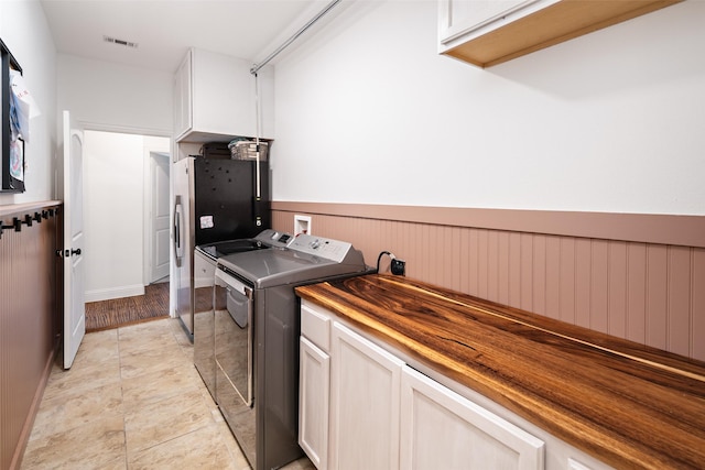 clothes washing area with washer and clothes dryer, cabinet space, and visible vents