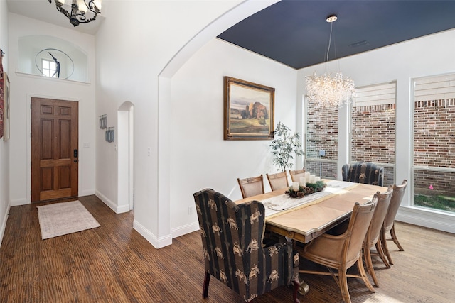 dining space featuring arched walkways, baseboards, wood finished floors, and a notable chandelier