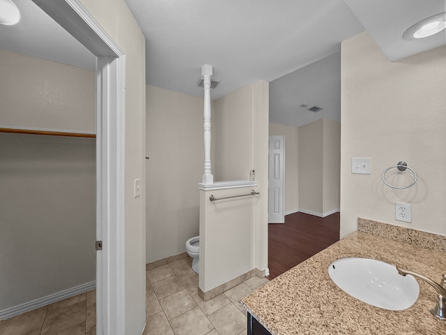 bathroom with visible vents, vanity, toilet, baseboards, and a spacious closet