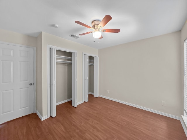 unfurnished bedroom with visible vents, multiple closets, wood finished floors, baseboards, and ceiling fan