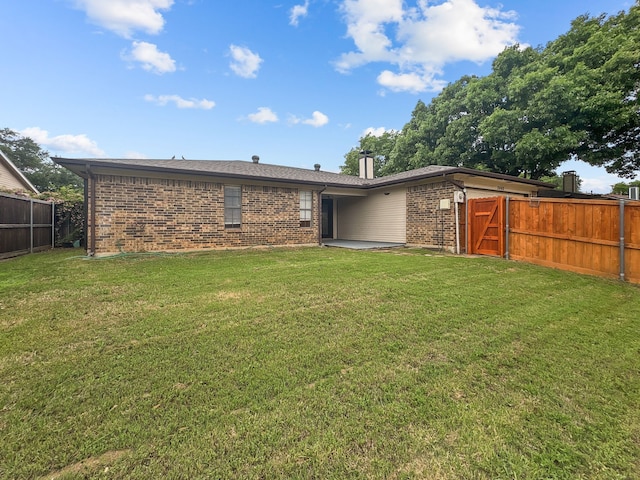 rear view of house featuring a fenced backyard, a chimney, a yard, and brick siding