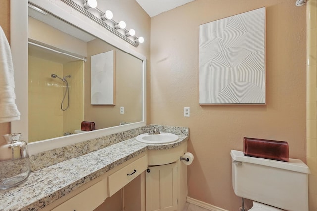 bathroom with vanity, baseboards, toilet, and tiled shower