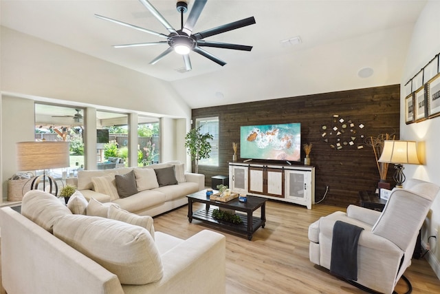 living area featuring wooden walls, a ceiling fan, high vaulted ceiling, and light wood-type flooring