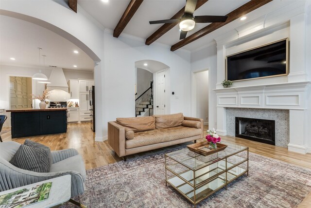 living room with a ceiling fan, beam ceiling, stairway, light wood-type flooring, and arched walkways