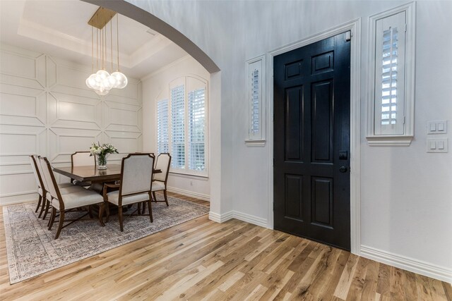 entryway featuring arched walkways, baseboards, a tray ceiling, and wood finished floors