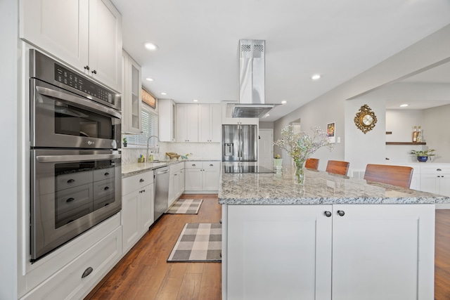kitchen featuring wood finished floors, a kitchen island, island range hood, white cabinetry, and stainless steel appliances